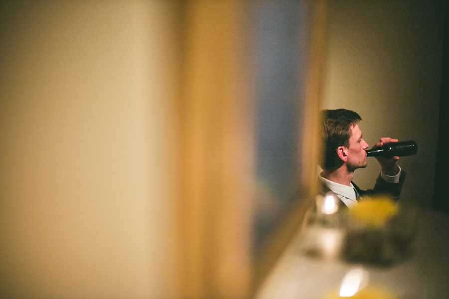 Adam and Beth, dressed to the nines, are all smiles and laughter as they sit against a brick wall at their wedding reception in the Fathom Gallery.
