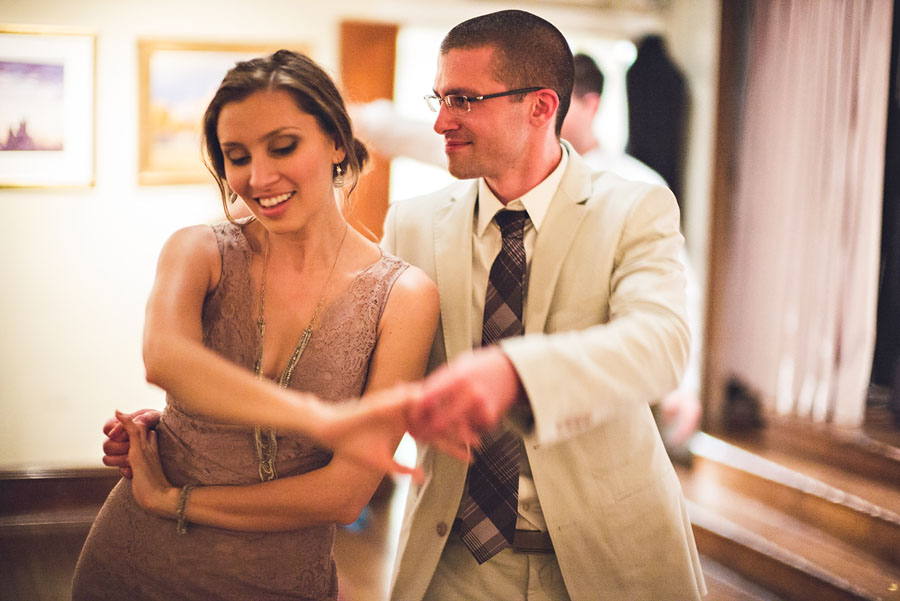 Black and white photo of three people sitting together, holding hands. The man in the center, Adam, wears glasses and a suit, flanked by two women on either side—one of them Beth—both looking at him. This intimate moment was captured beautifully during a Fathom Gallery Wedding.