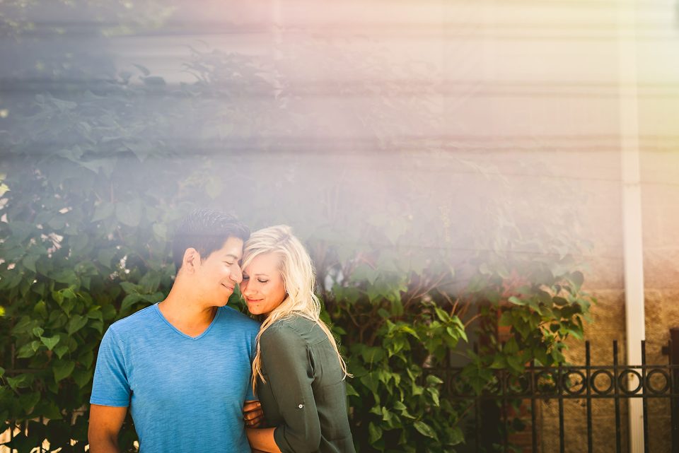 A couple stands close together, smiling, in front of a sunlit wall covered with green ivy, captured through the creative technique of prisming photography.