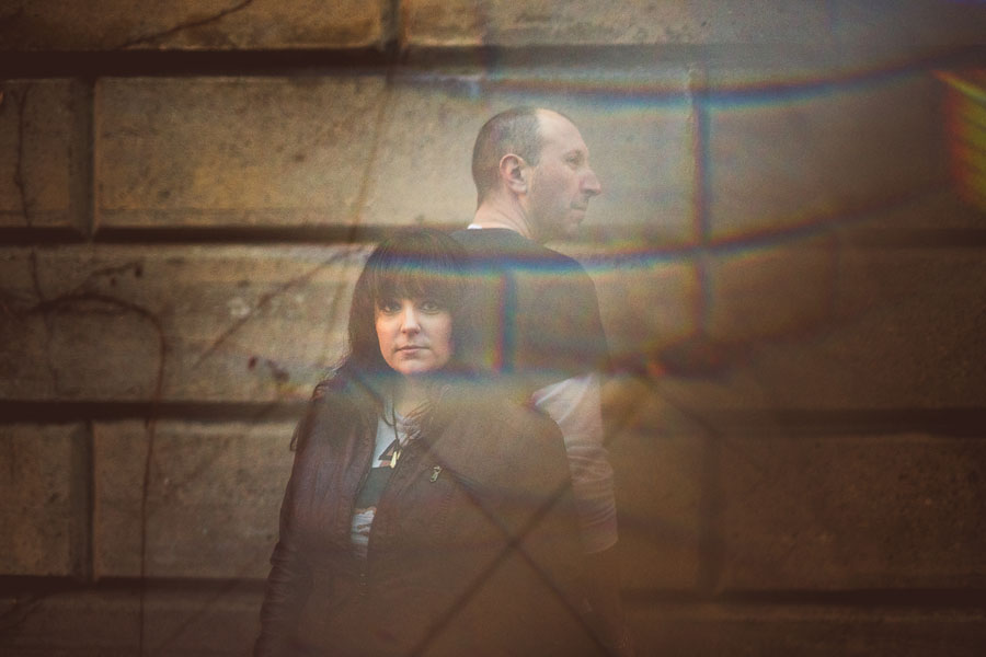A man and woman standing against a stone wall, partially obscured by colorful prisming.