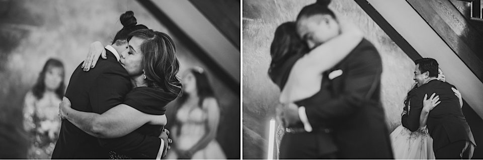 Black and white image of two people embracing in an emotional hug at an NYC wedding, with out-of-focus figures in the background.