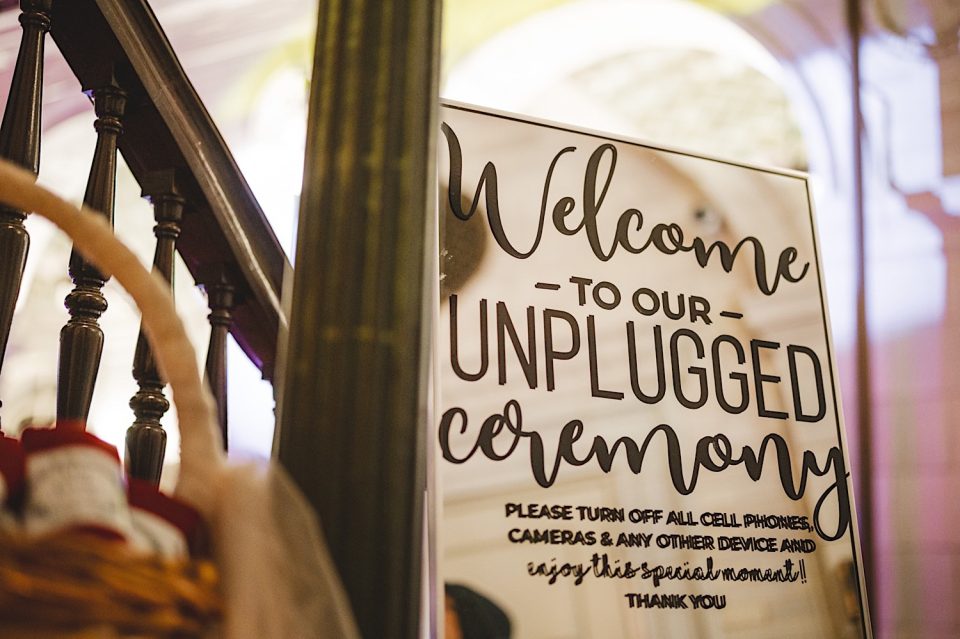 A sign at John Boathouse for a NYC Wedding reads "Welcome to our Unplugged Ceremony" asking guests to turn off all electronic devices to enjoy the moment.