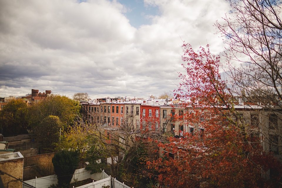 Aerial view of a boathouse wedding in a residential neighborhood with rows of red brick buildings under a cloudy sky, framed by autumn trees.