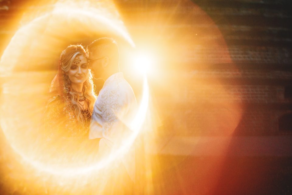 A couple in traditional South Asian attire embracing, with a golden sunlight flare encircling them, captured in a Nikon Z9 review.