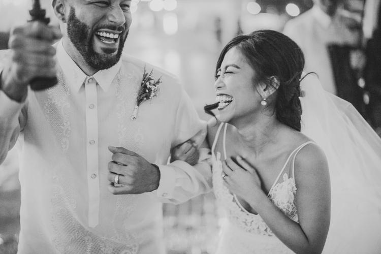 A bride and groom smile and laugh joyfully, holding hands and embracing each other during their wedding celebration, captured beautifully with a Canon EOS R.