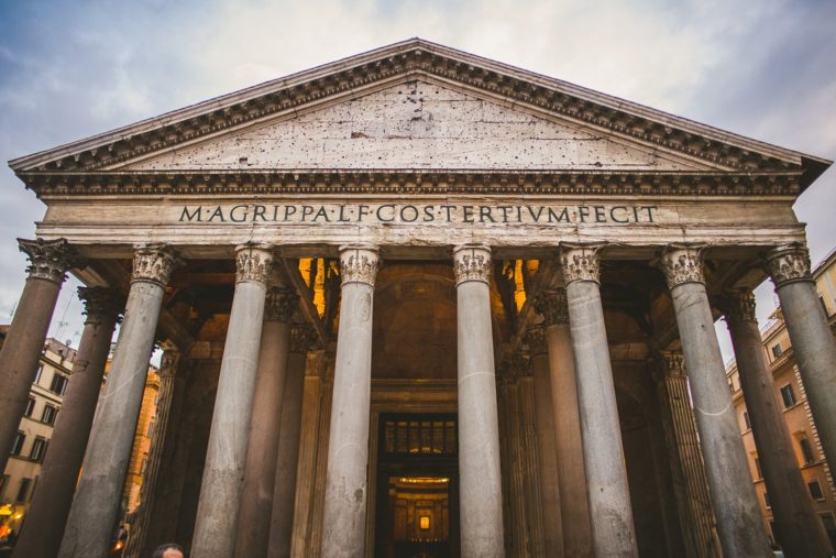 Wide-angle view of the Pantheon in Rome, showcasing its grand columns and ancient inscription under a cloudy sky.