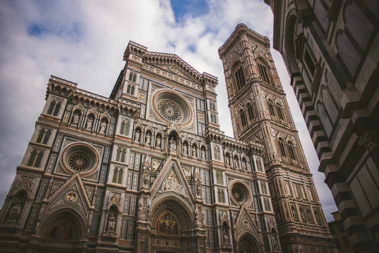 Exterior view of Florence Cathedral with its intricate marble facade and towering bell tower against a cloudy sky.