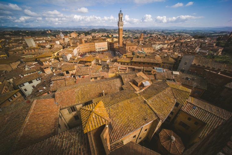 Aerial view of Siena, Italy, showcasing terracotta rooftops and the iconic Torre del Mangia.