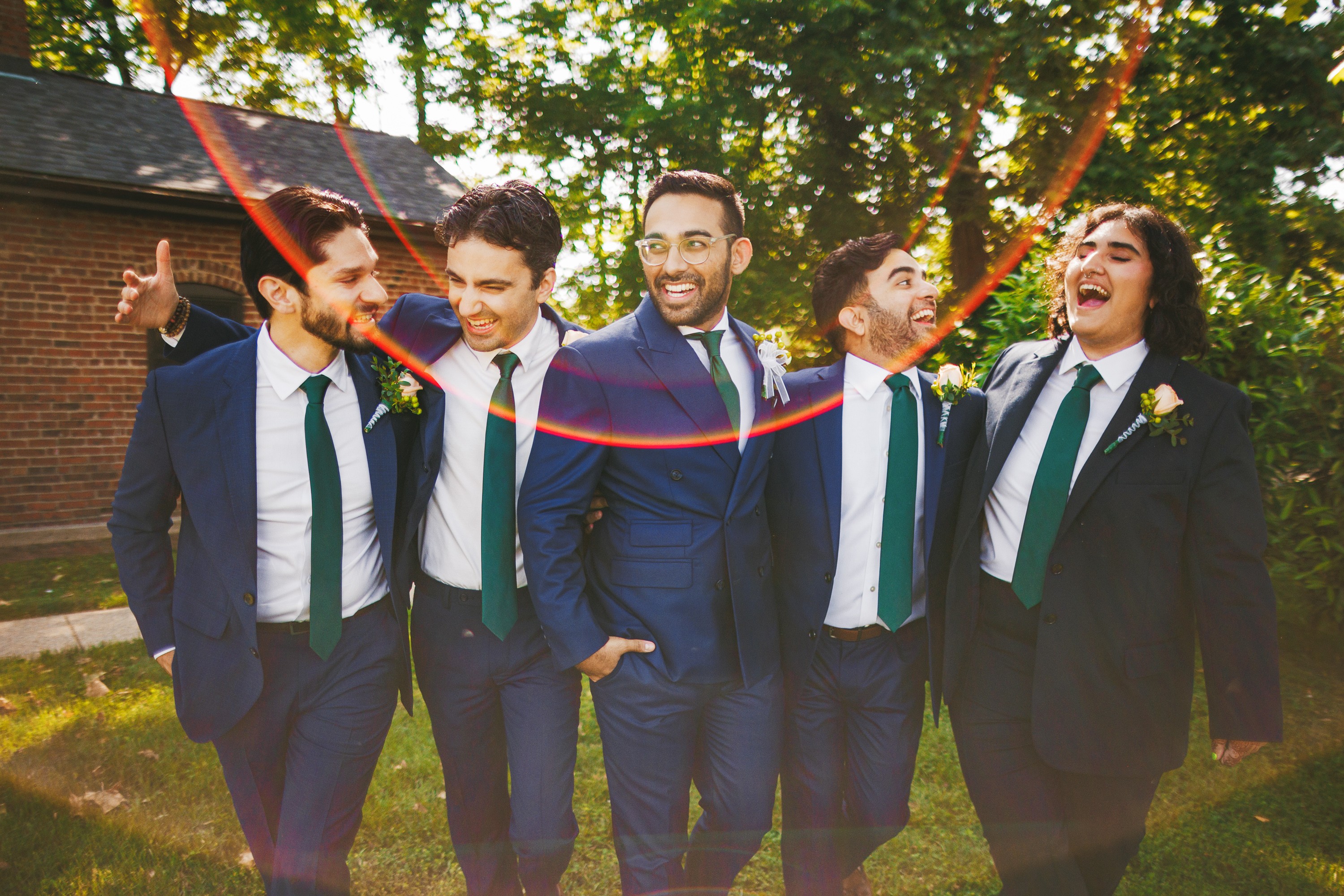 Five men in suits with green ties stand closely together, smiling and laughing, outside on a sunny day, their camaraderie as seamless as an auto draft.