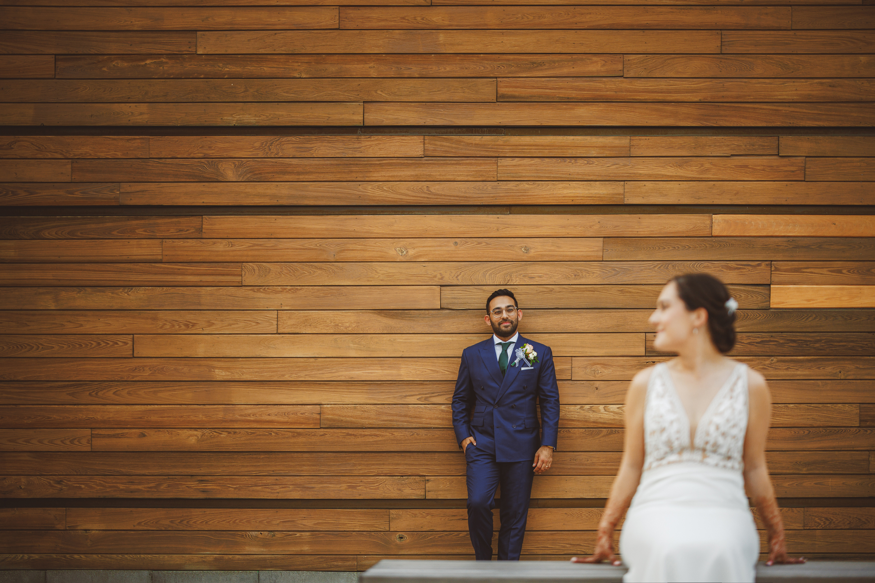 A man in a blue suit leans against a wooden wall, while a woman in a white dress sits in the foreground, slightly out of focus. It’s as if they’re part of an Auto Draft sequence, capturing moments yet to be finalized.