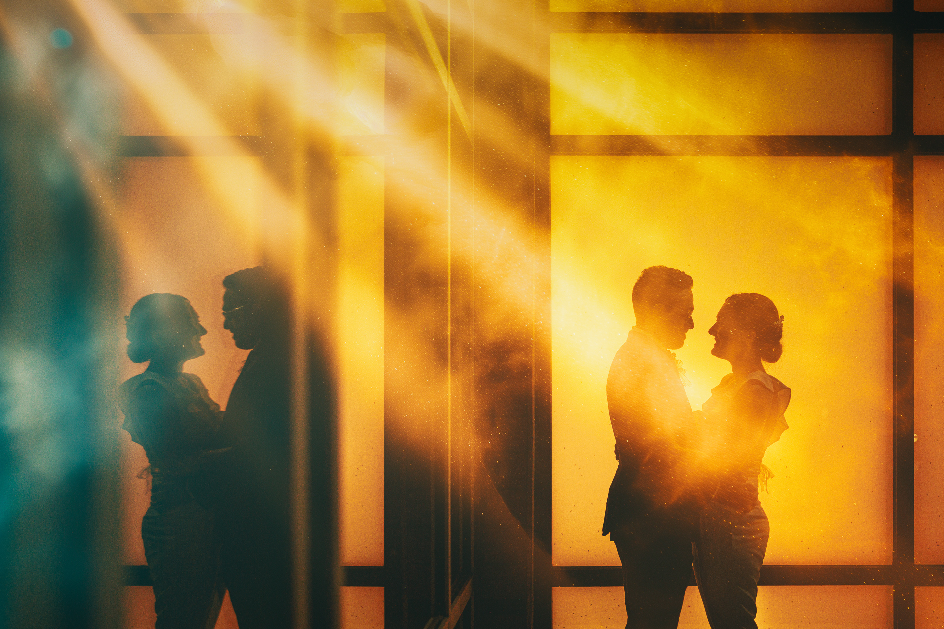 Silhouettes of two couples standing face to face, illuminated by warm golden light with reflections creating a mirrored effect—an auto draft of fleeting yet profound moments etched in time.