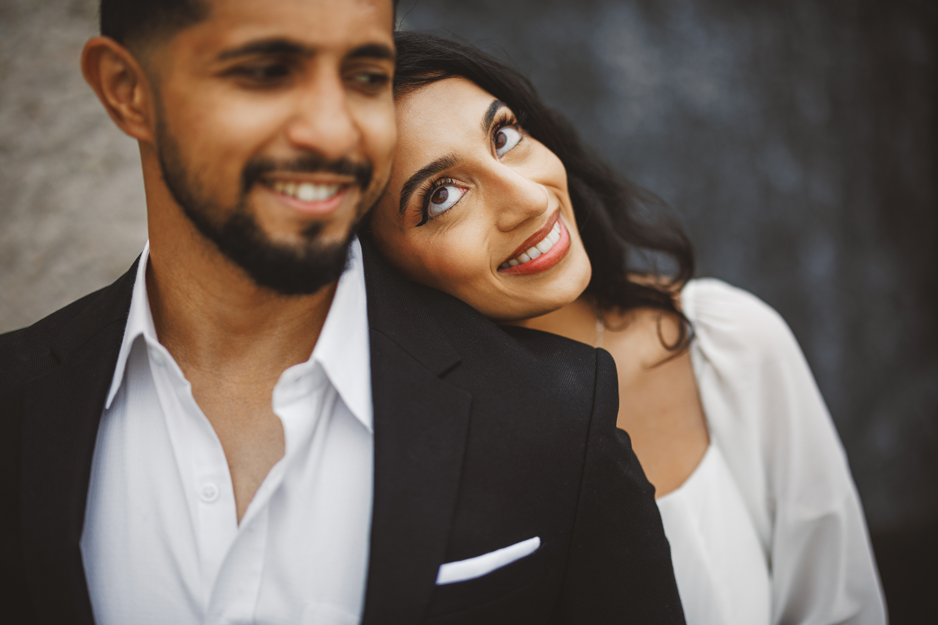 A smiling woman leans her head on a smiling man's shoulder. Both are dressed in casual formal attire, with the man in a black blazer and white shirt, and the woman in a white dress. It's almost as if their perfect moment was picked through precise keyword selection.