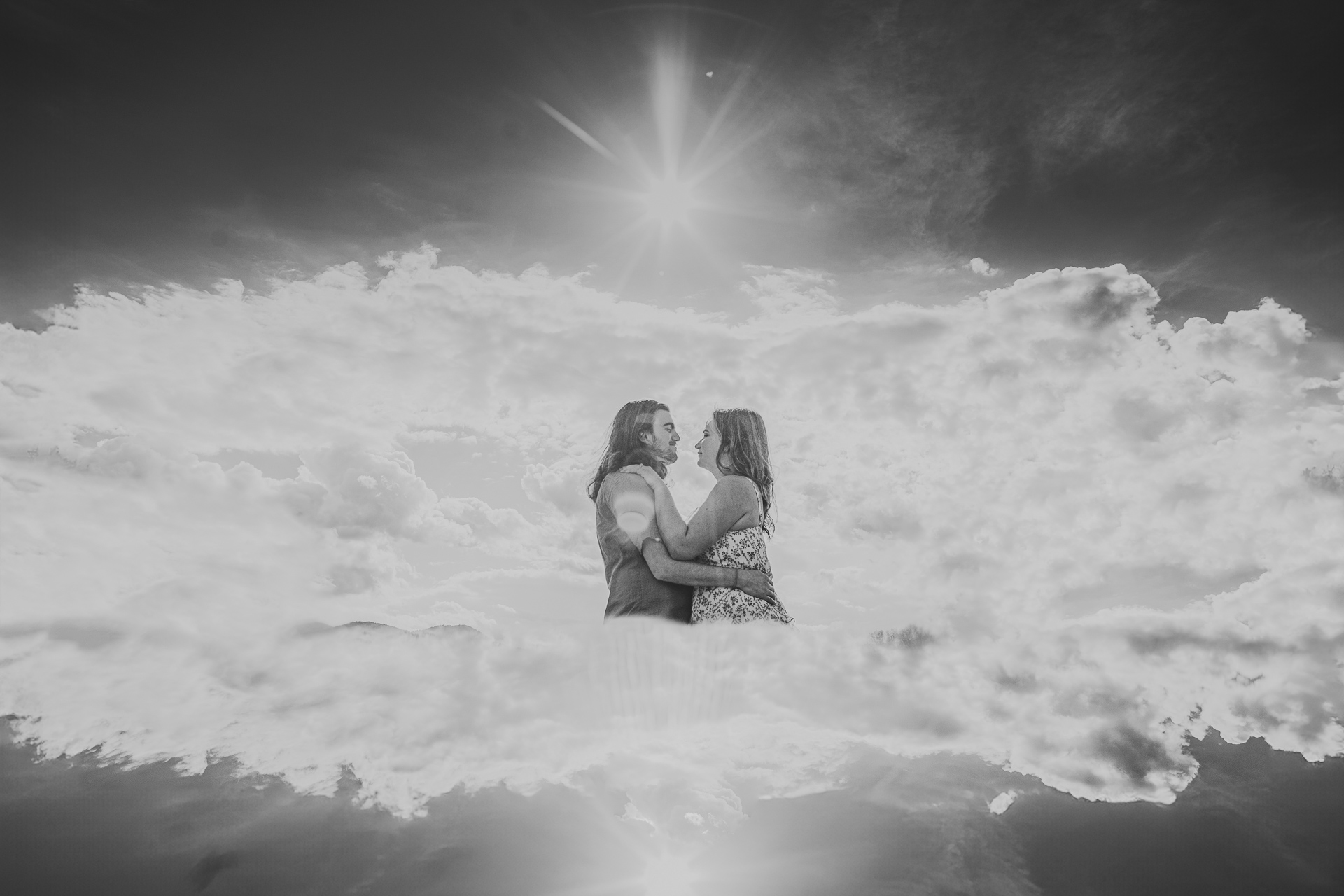 A black-and-white image of a couple embracing within a surreal scene of floating clouds and a bright sunburst above them, as if captured in an ethereal auto draft.