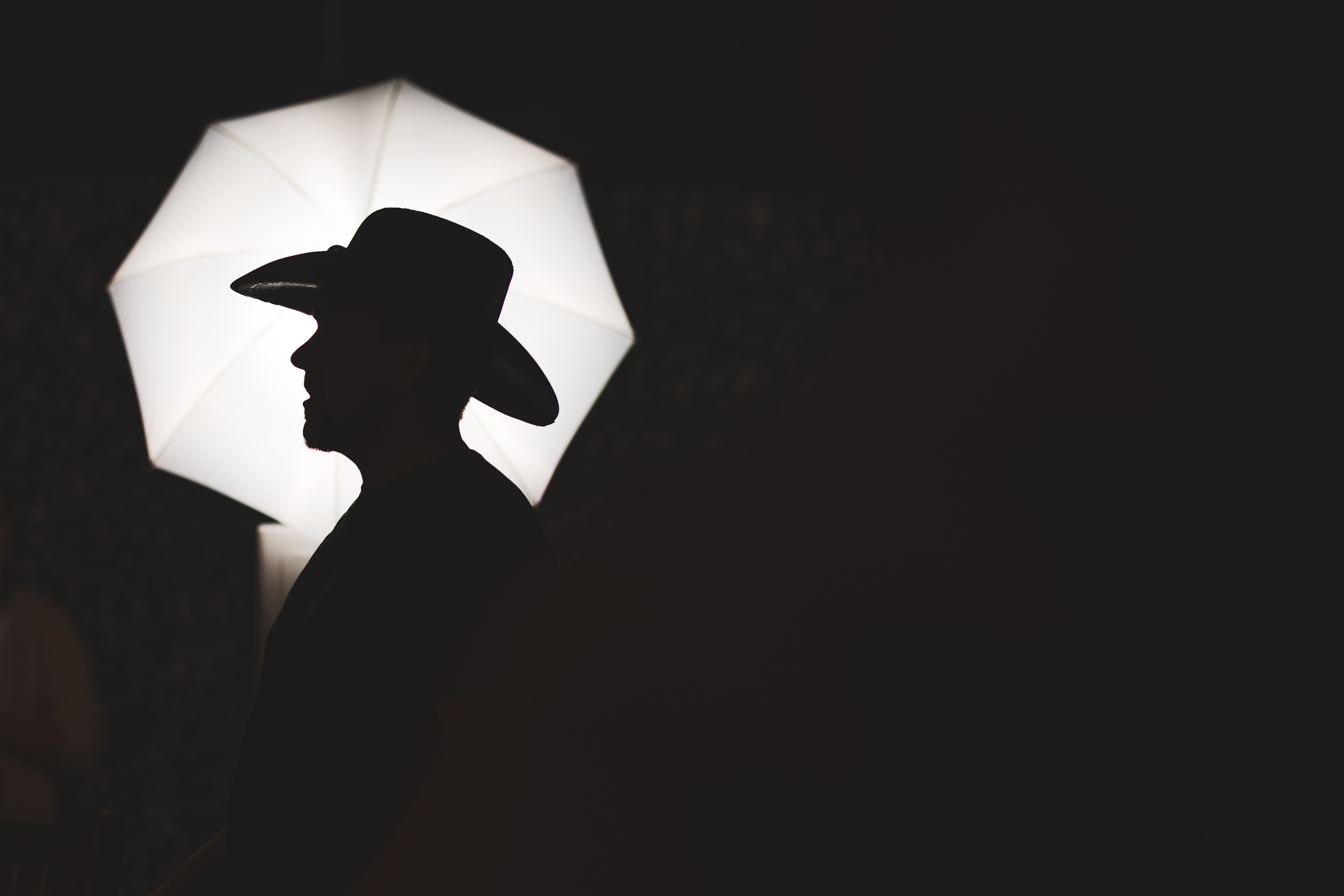 Auto Draft: Silhouette of a person wearing a hat against a bright, umbrella-shaped light source in a dark environment.