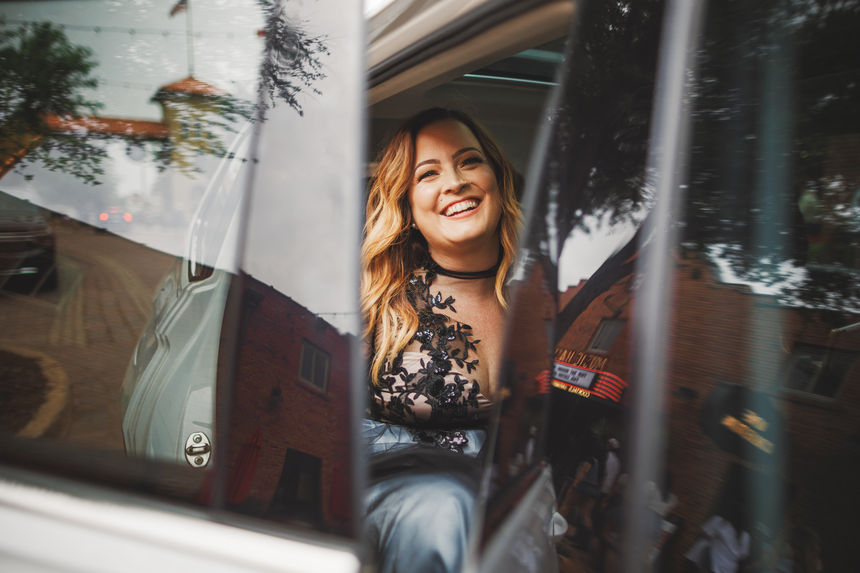 A woman in a black floral top smiles while sitting in the backseat of a car with the door open, as if posing for an auto draft.