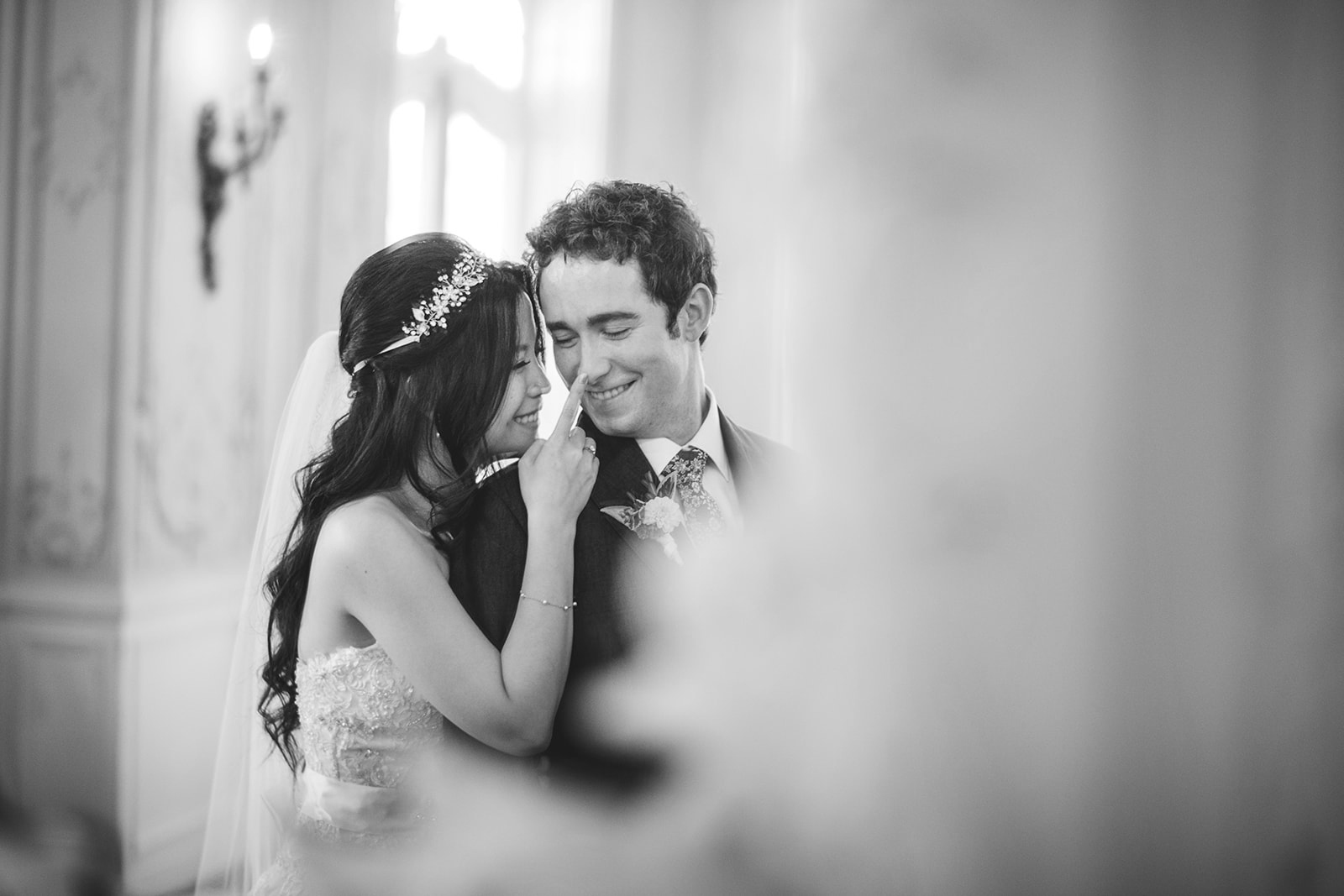 In an elegantly decorated room, a bride and groom share an intimate moment in a black-and-white photo. The bride gently touches the groom's face, both smiling blissfully, while the photographer captures this perfect scene with no need for Auto Draft.