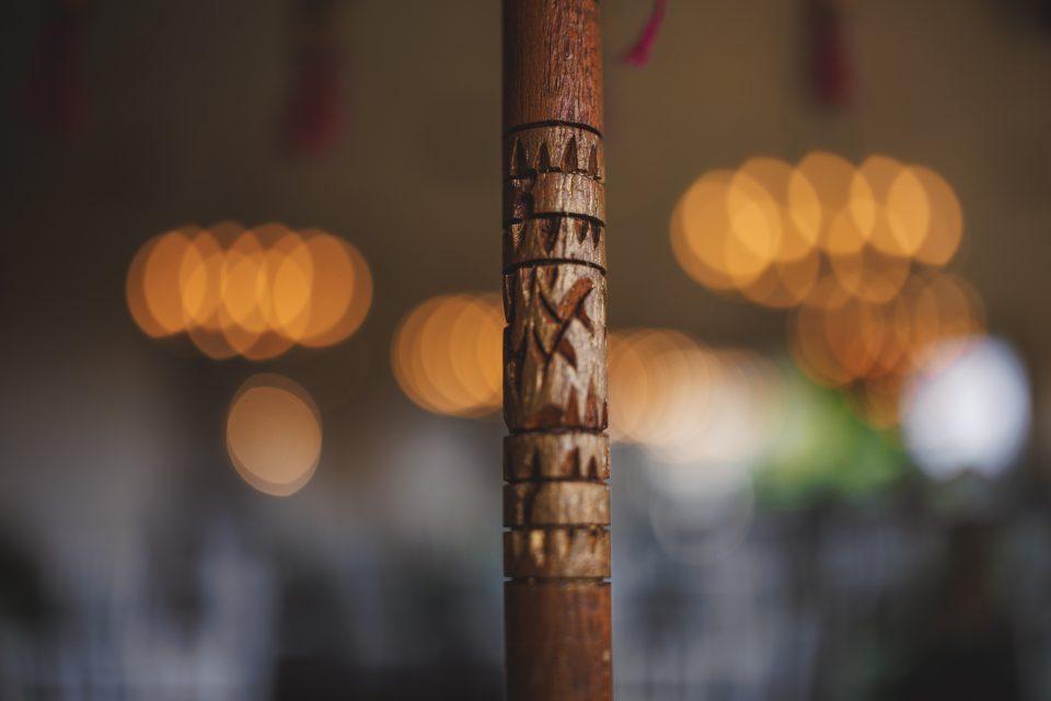A close-up of a carved wooden pole with bokeh lights in the blurred background.