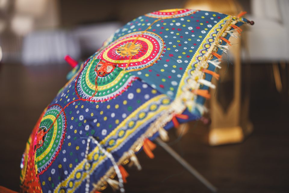 A colorful, ornate umbrella with intricate embroidery and vibrant patterns lies tilted on a wooden floor indoors.