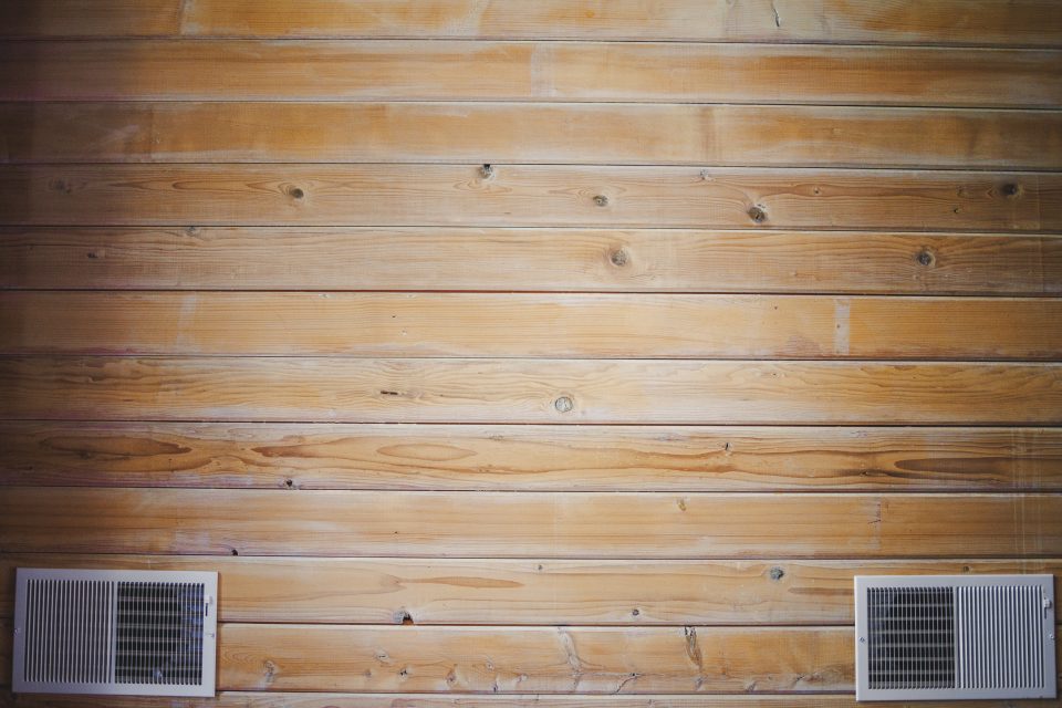 Close-up of a wooden wall with a horizontal panel design, featuring two white air vents placed near the bottom, captured beautifully using the Canon 35 1.4 VCM lens.
