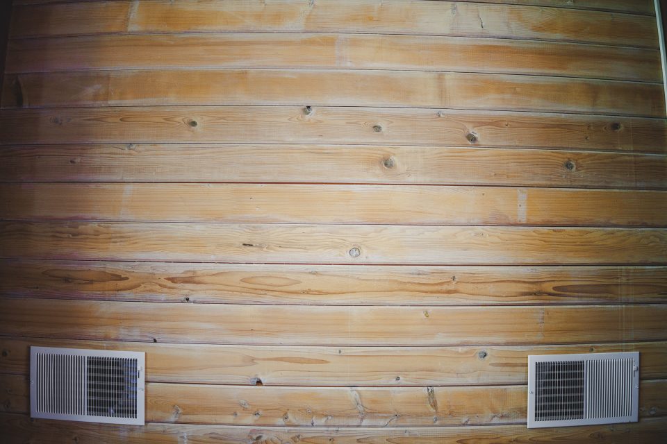 Wooden wall with horizontal planks captured beautifully with the Canon 35mm 1.4 VCM lens review, showcasing two rectangular air vents near the bottom.