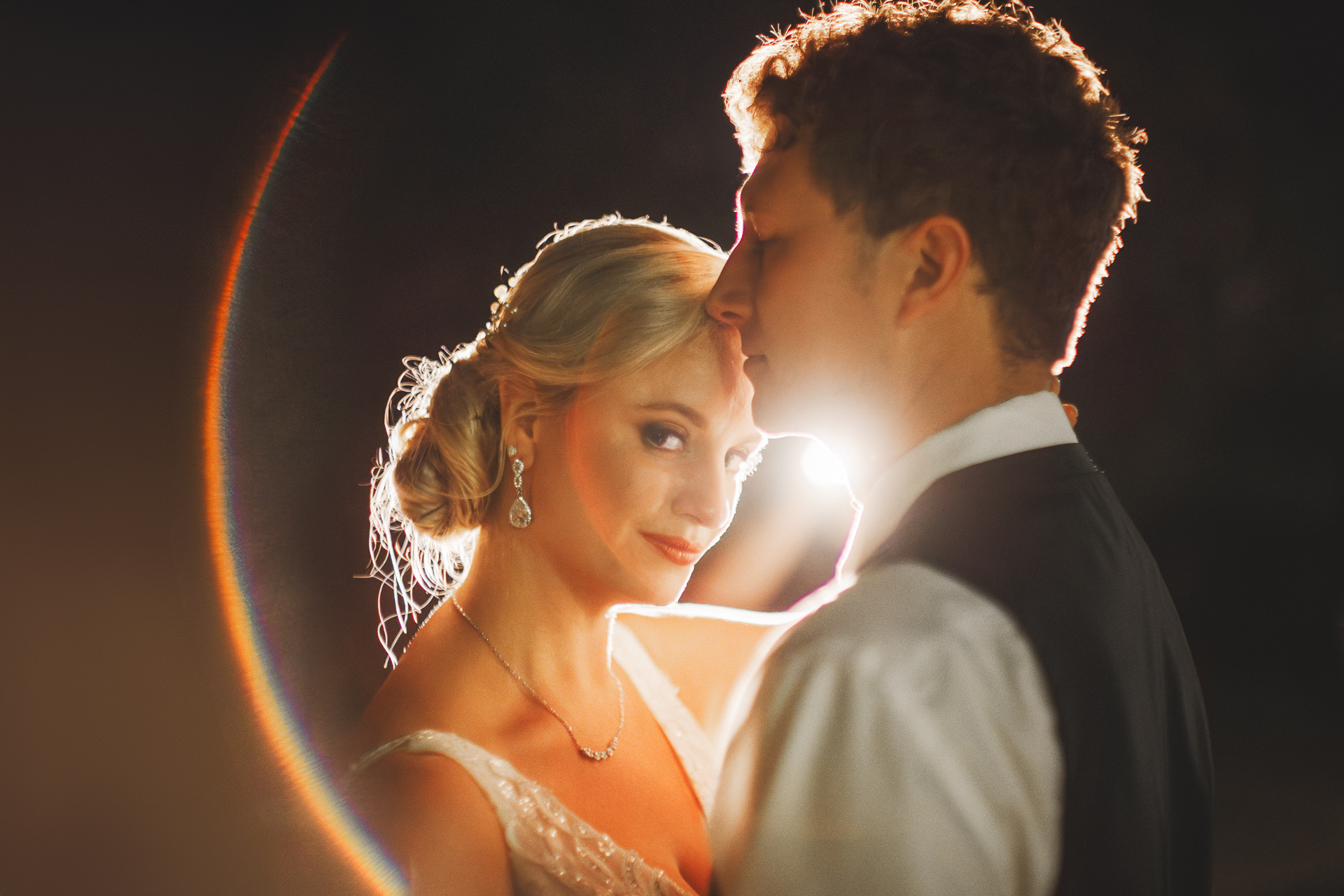 A couple in formal attire embraces under a soft, glowing light, Auto Draft highlighting the woman's earrings and hairstyle, and the man's profile.