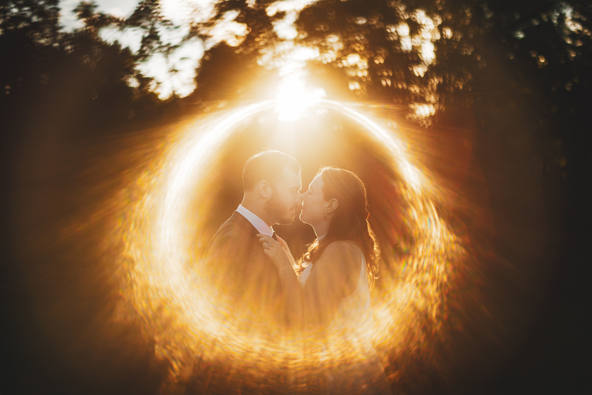 A couple is standing close, bathed in warm sunlight with a lens flare creating a circular light effect around them, as if captured by an auto draft. Trees are visible in the background.