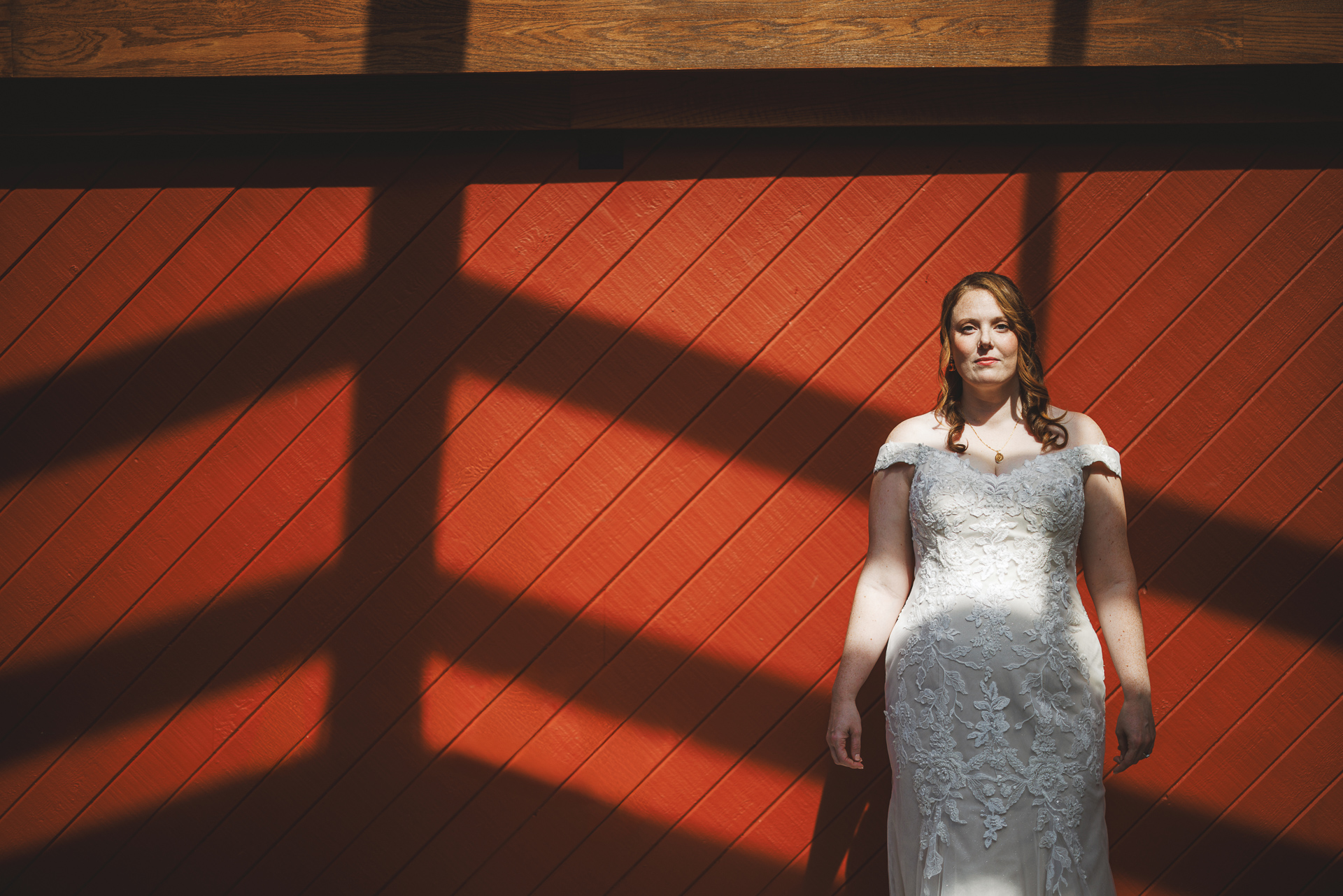 A woman in a white dress stands against a red wall, shadows cast in intersecting lines resembling an auto draft pattern.