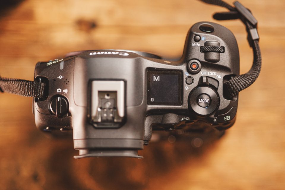 Top view of a Canon DSLR camera displaying various buttons, dials, and the LCD screen on a wooden surface, perfect for those interested in a Canon R5 Mark ii Review or understanding real-world use.