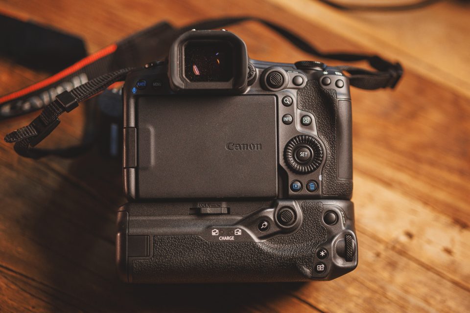A DSLR camera with a battery grip attachment rests on a wooden surface. The back view shows the screen and various control buttons, exemplifying a Canon R5 Mark ii Review. This setup, ideal for real-world use, has captured over 17k images flawlessly.