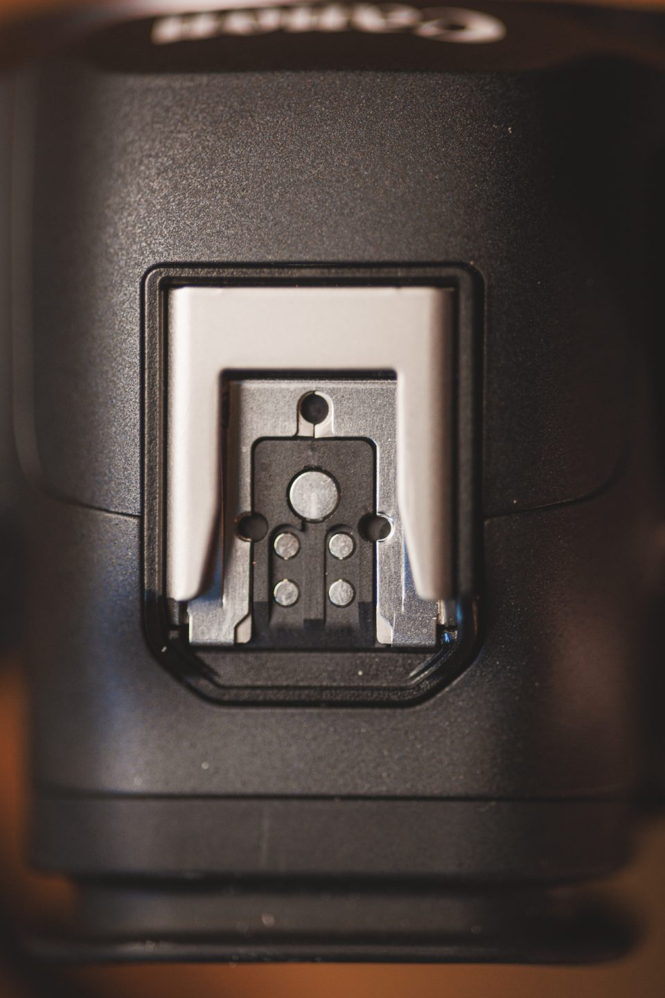 Close-up of a camera's hot shoe mount, which is used for attaching accessories such as external flashes. The mount features a metal contact plate and alignment pins within a rectangular housing.