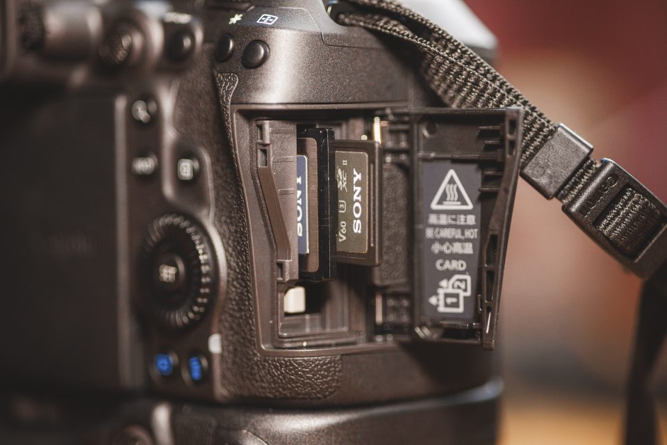 Close-up of an open camera card slot revealing two inserted memory cards. The camera strap and various buttons are partially visible around the card slot.