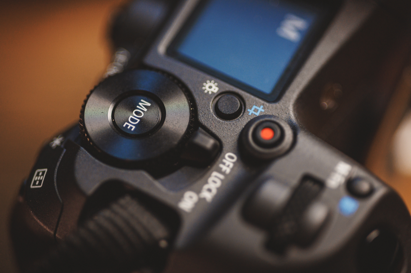 Close-up of a digital camera's mode dial and various control buttons, including an ON/OFF switch and a red button, as highlighted in the Canon R5 Mark ii Review for its impressive performance in real-world use.