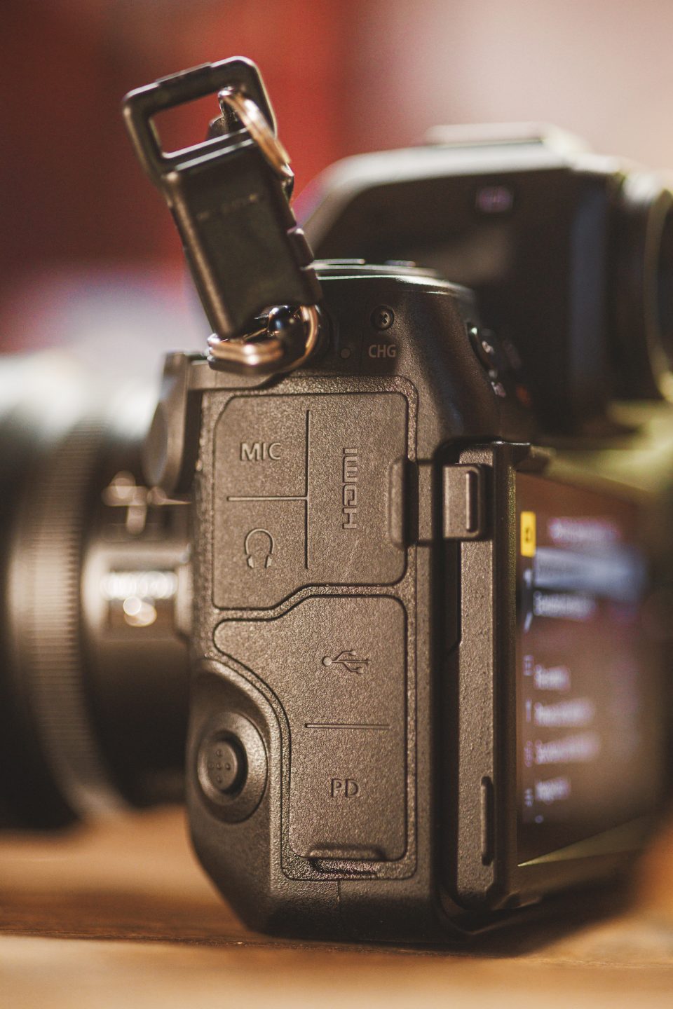 Close-up of a digital camera with Auto Draft mode, focusing on side ports labeled MIC, HDMI, USB, and PD. A strap is attached to the top while the screen displays a blurred menu.