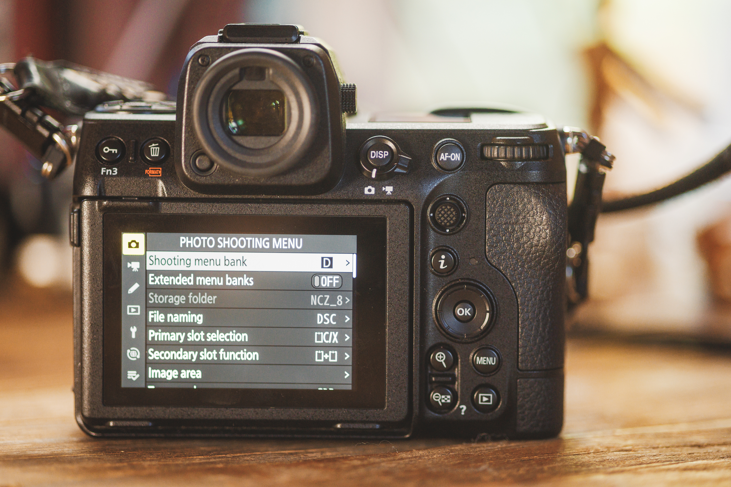 A digital camera rests on a wooden surface, with the photo shooting menu and Auto Draft options prominently displayed on its screen.