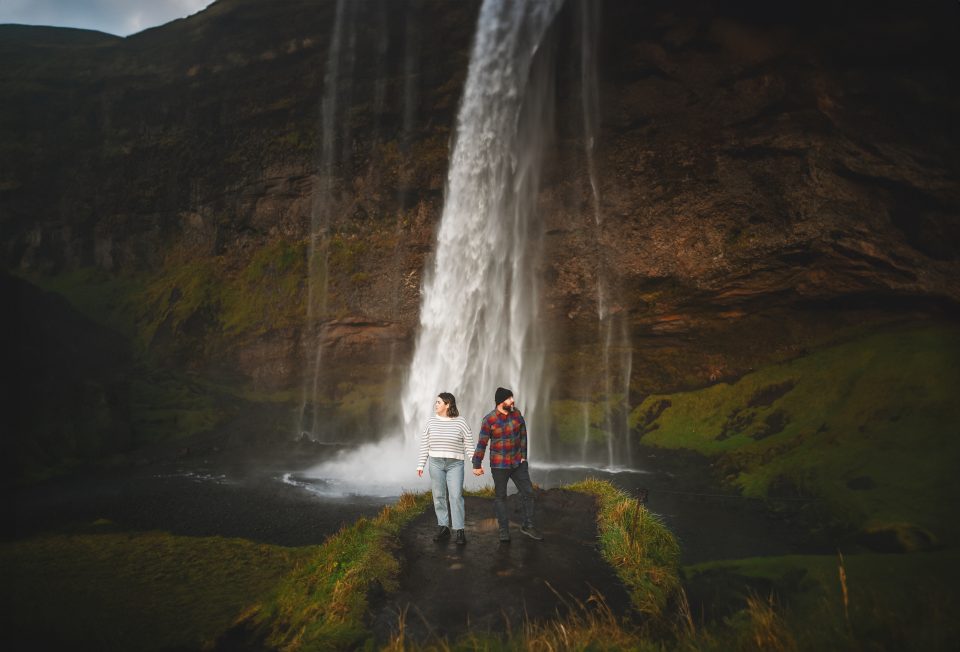 Two people stand together on a path in front of a cascading waterfall, auto-drafting their journey through the lush greenery.
