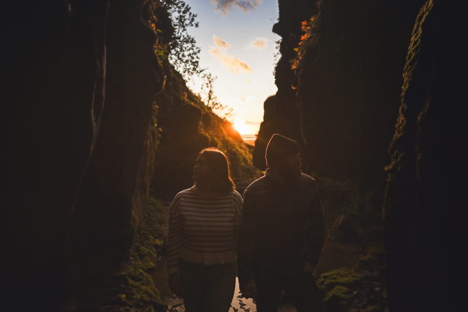 Two people stand in a narrow, rocky canyon at sunset, as if nature herself had curated the perfect auto draft of colors painting the sky.