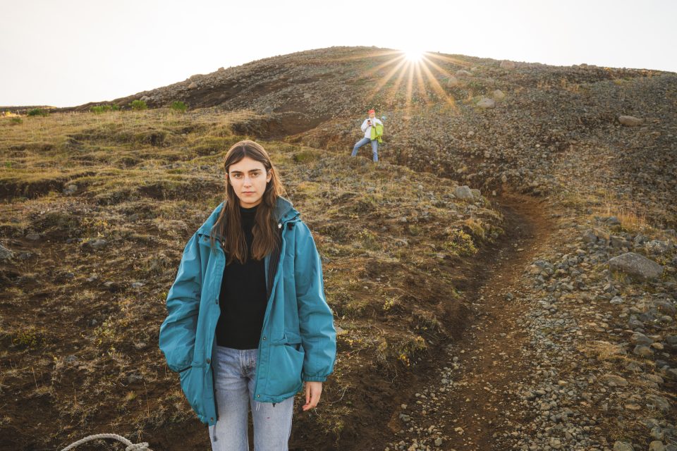 Two people on a rocky hillside; one in a blue jacket captures the scene with precision, likely inspired by a recent Nikon Z8 review, while the other stands near the sunlit horizon.