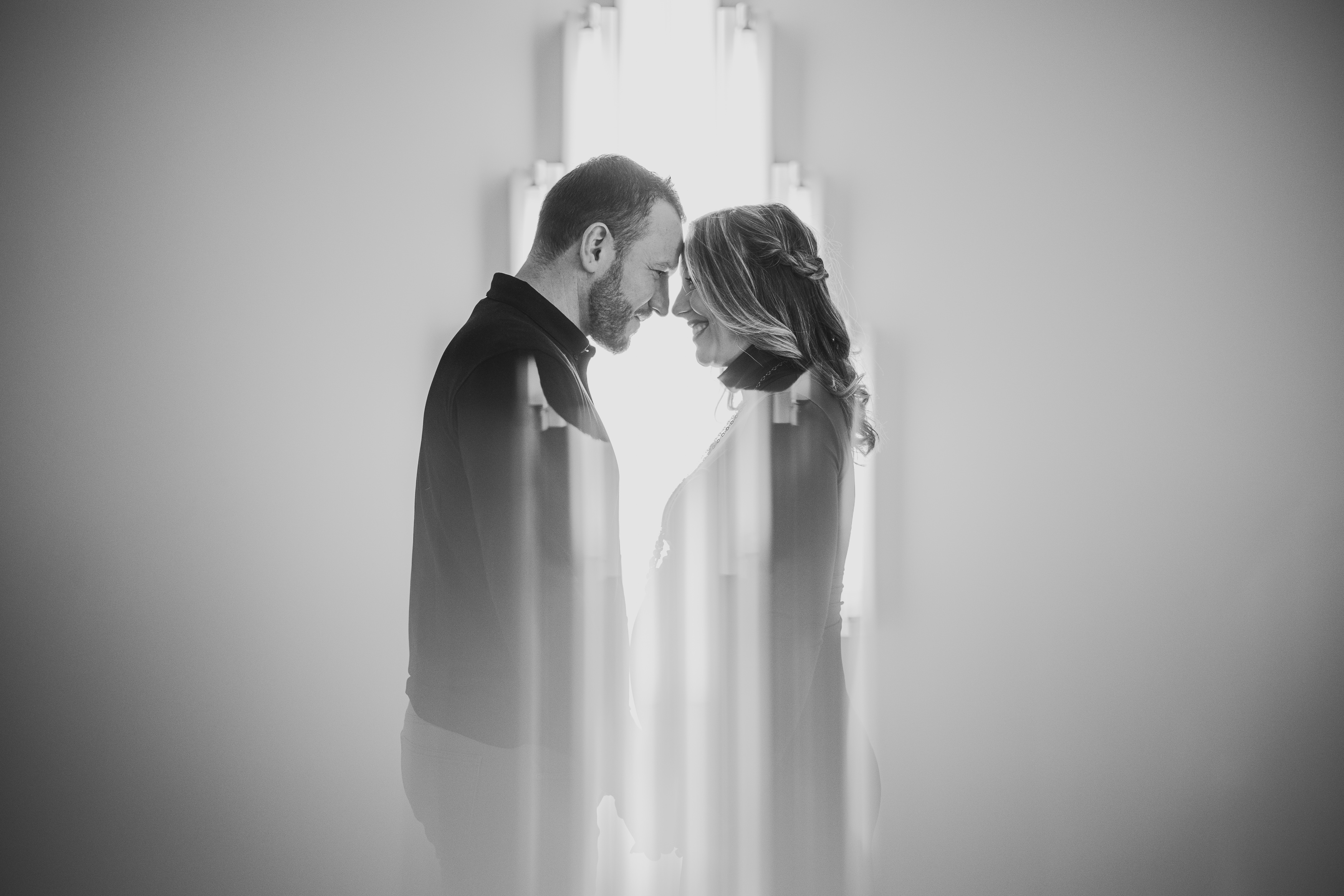 A man and woman stand closely facing each other, smiling. The image is black and white with a soft, blurred effect.