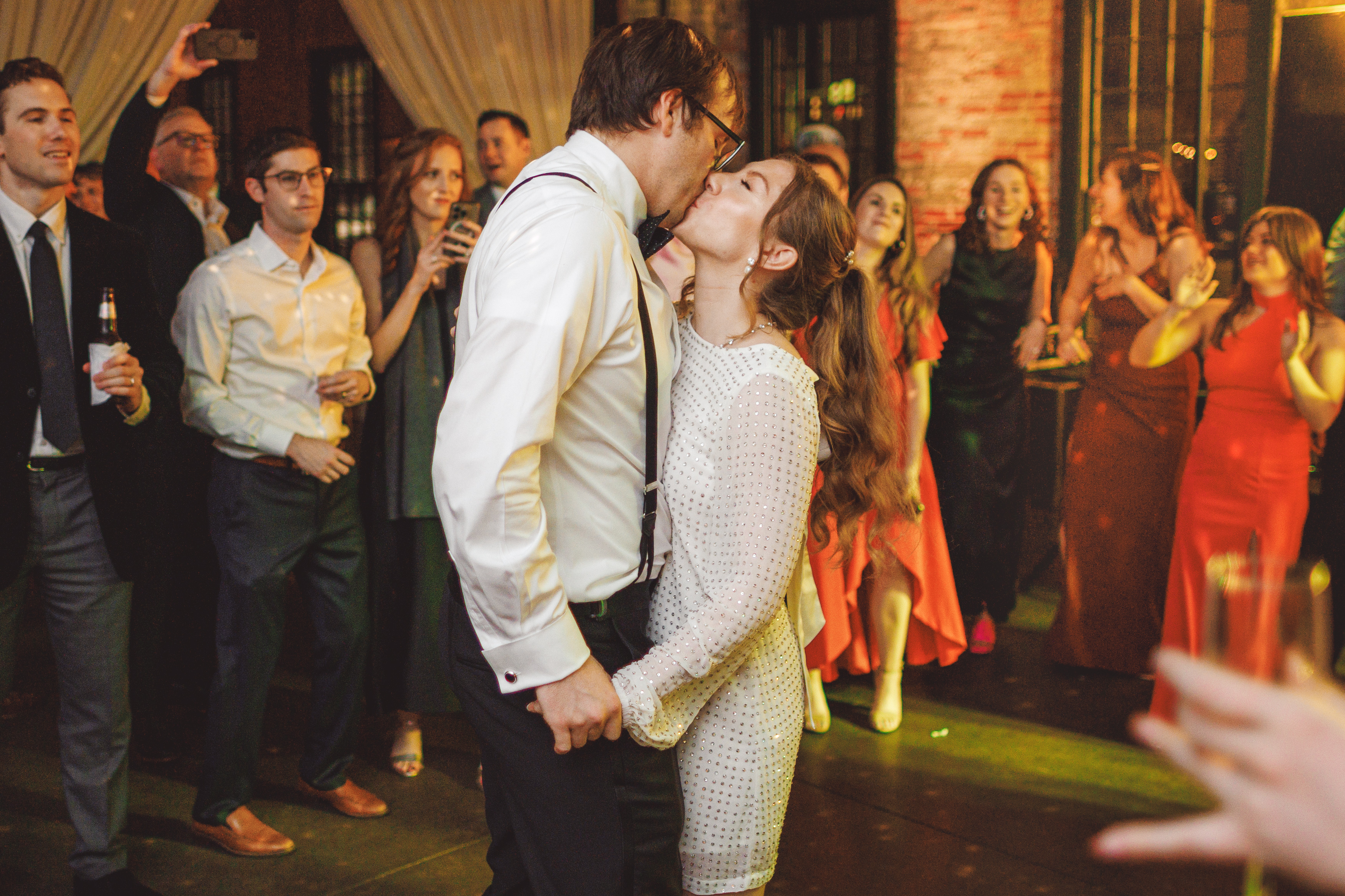 A couple kisses on the dance floor at a party, surrounded by cheering people.