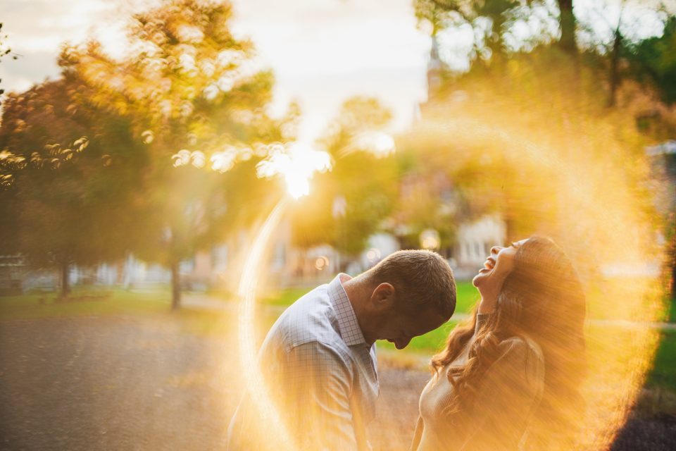 A man and a woman laugh together in a park with sunlight and blurred effects creating a golden halo around them.