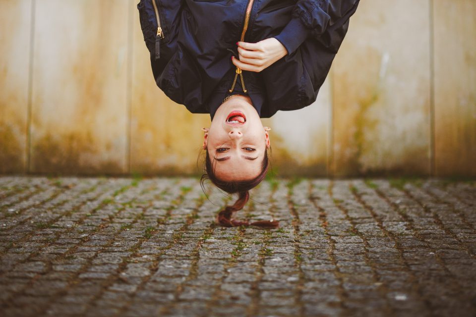 Person hanging upside down with a zipper coat in front of a textured stone wall.