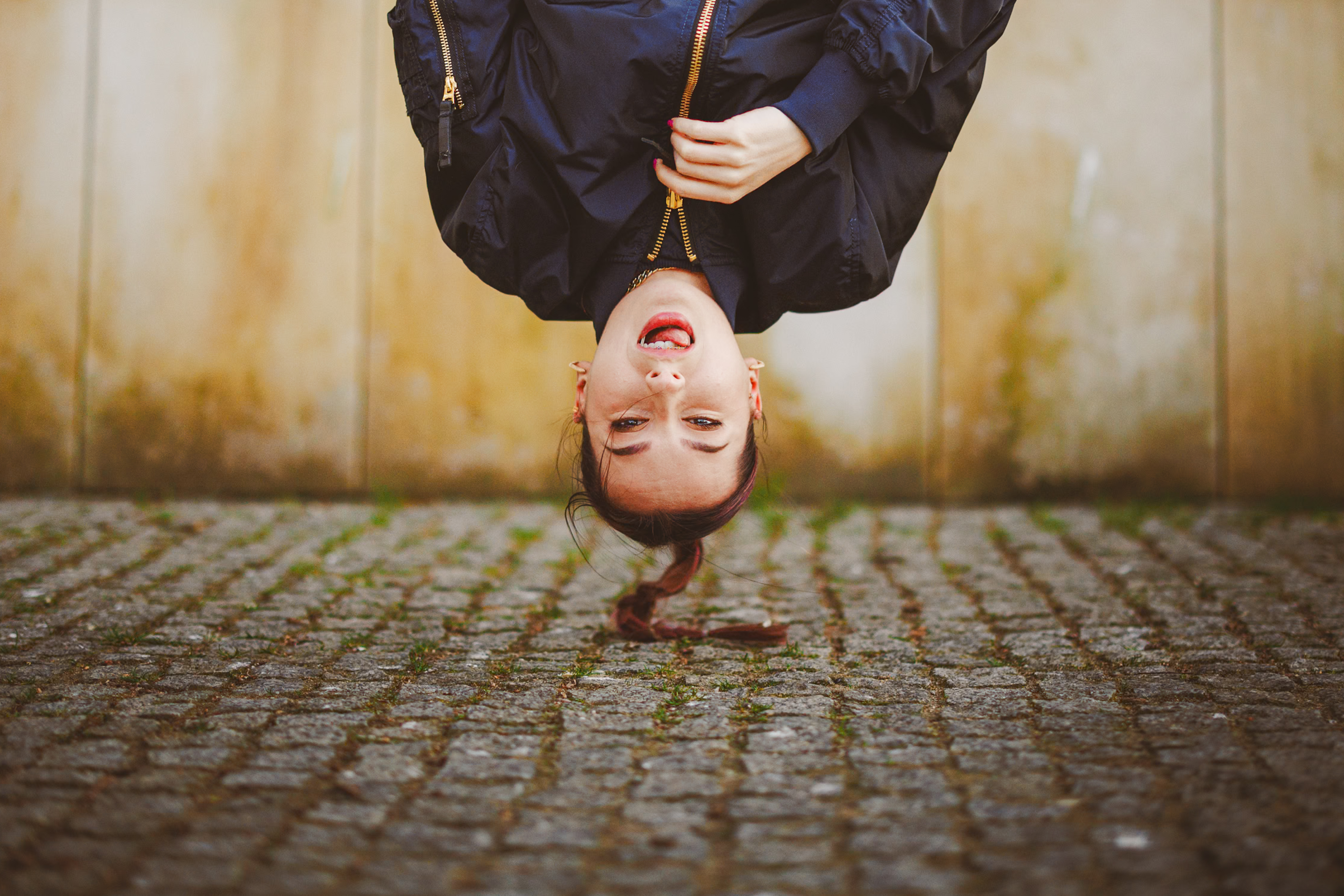 Person hanging upside down with a zipper coat in front of a textured stone wall.