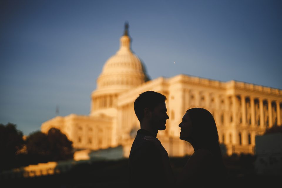 Silhouetted couple stands in front of the U.S. Capitol building at sunset.