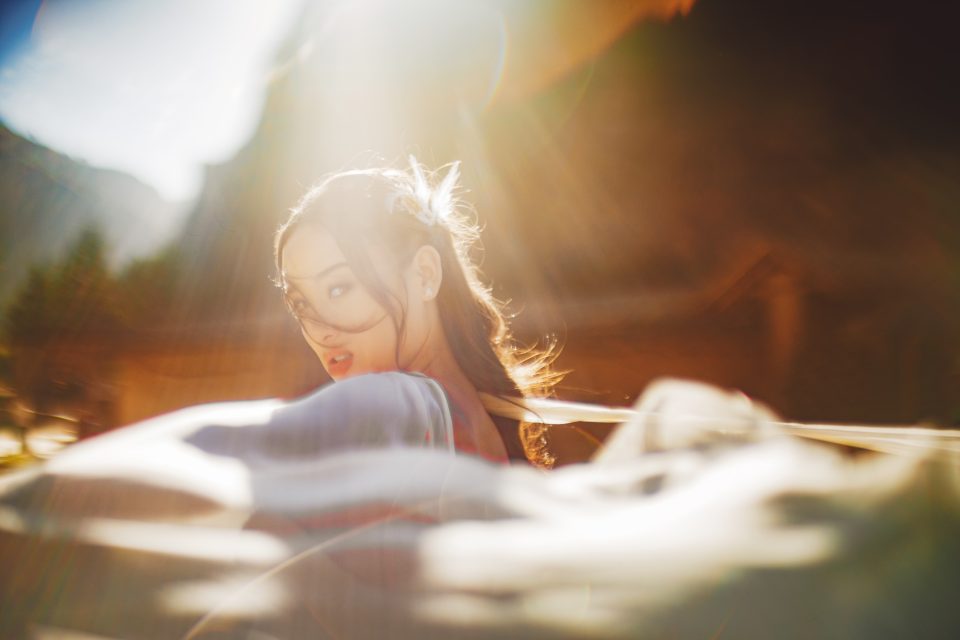 Person with long hair looks back over their shoulder, captured in soft golden light, with blurred fabric in the foreground.