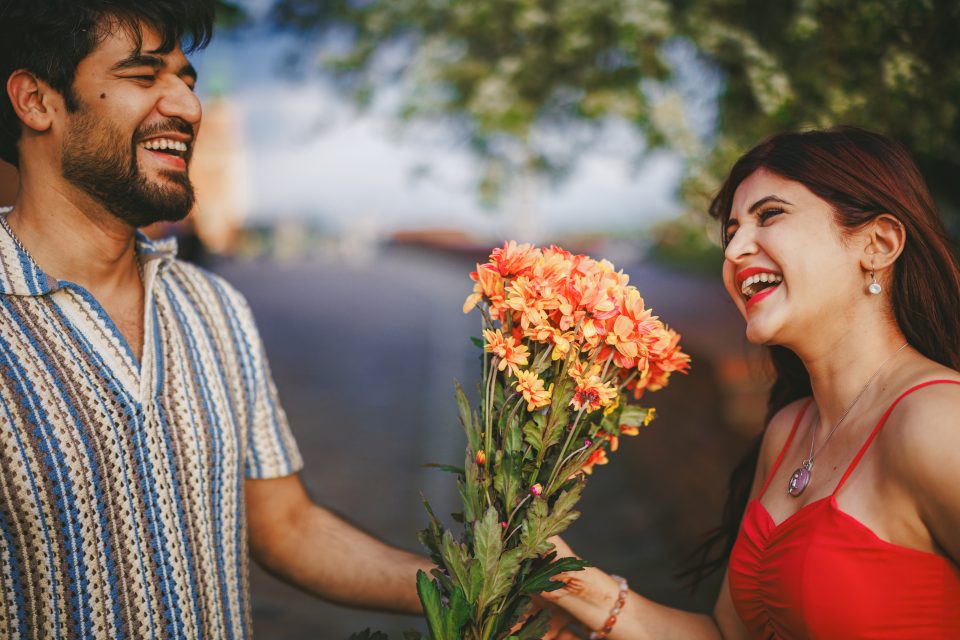 Two people smiling and holding a bouquet of orange flowers outdoors.