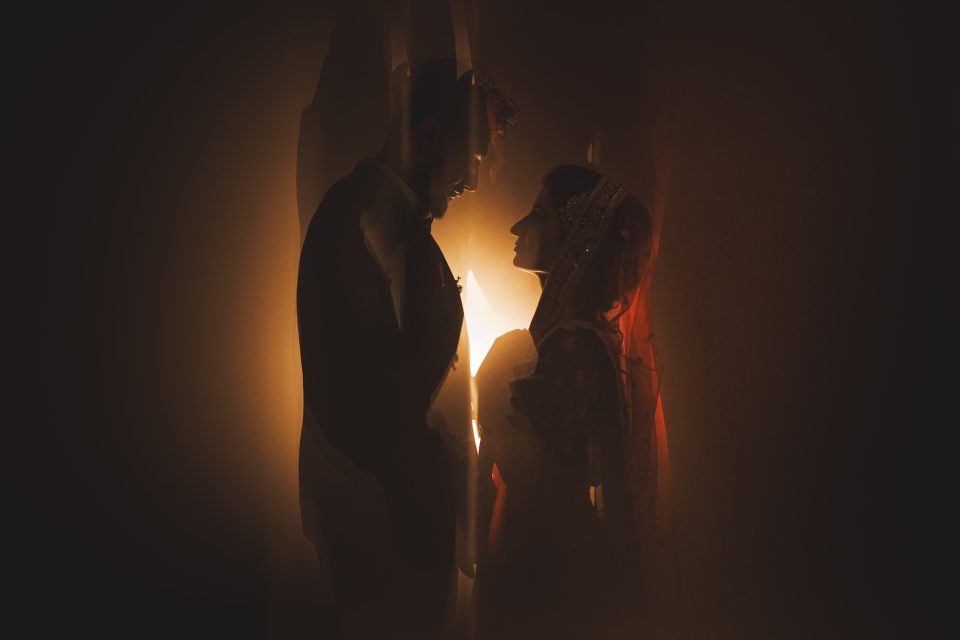 Silhouetted couple facing each other, surrounded by warm light, creating a romantic and intimate atmosphere.