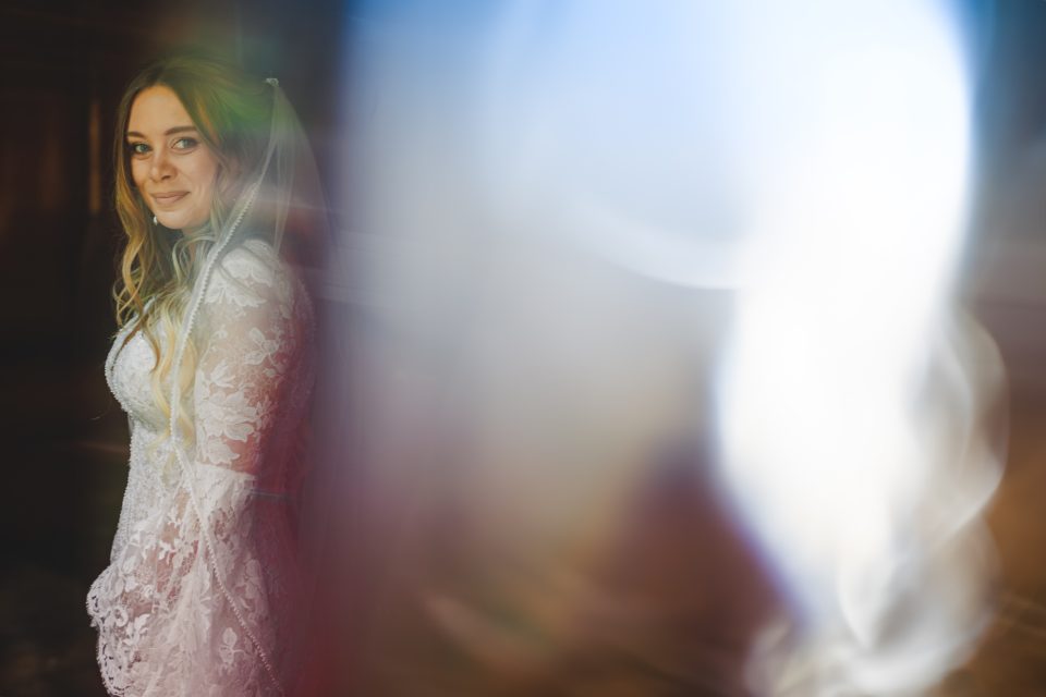 Bridal portrait featuring a woman in a lace wedding dress, partially obscured by soft, colorful light.