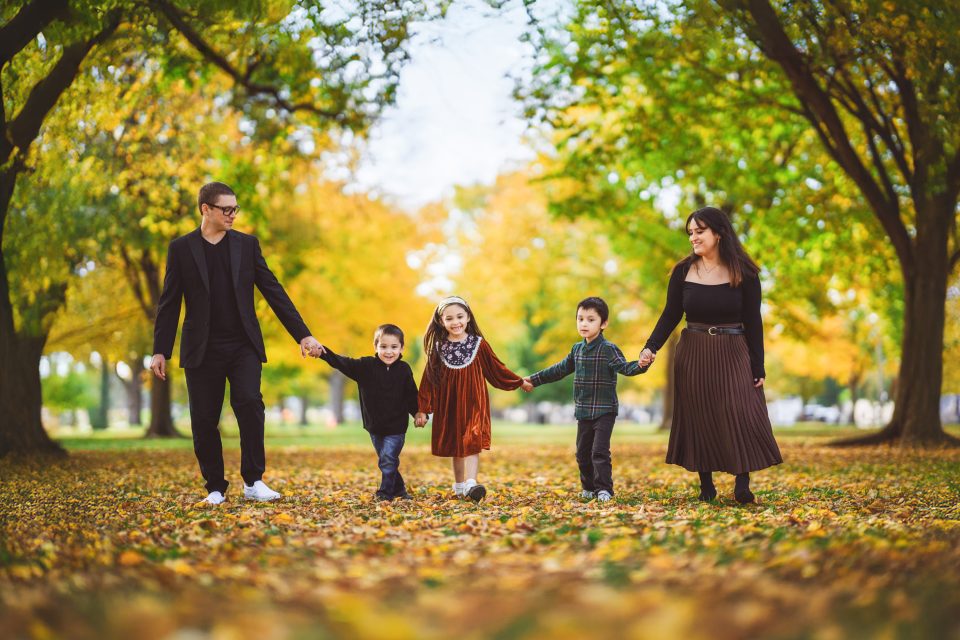 Family of five walking hand in hand under tree canopy in autumn.