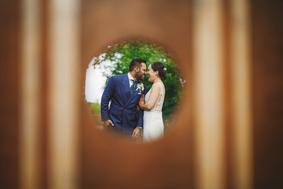 A bride and groom kiss, framed by a circular wooden opening.