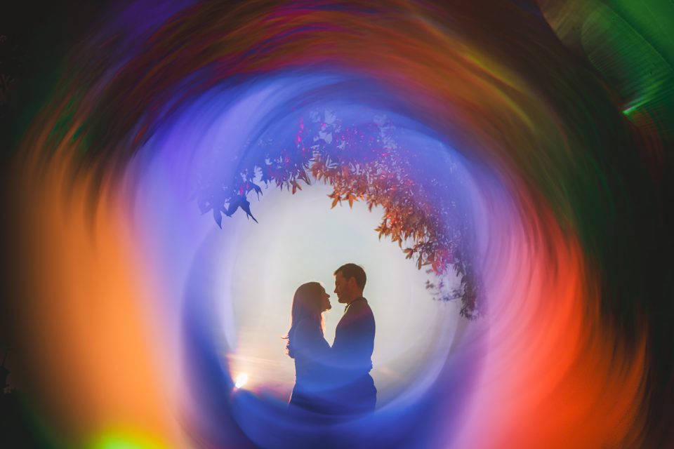 Silhouetted couple facing each other, surrounded by a colorful, swirling pattern with trees visible through the center.
